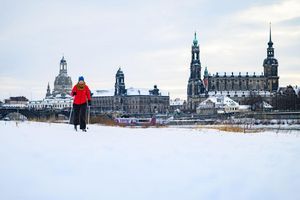 Eine Frau läuft am verschneiten Elbufer vor der historischen Altstadtkulisse in Dresden Ski - Foto: Robert Michael/dpa
