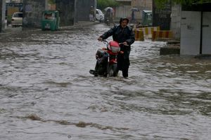 Ein Pakistaner watet nach starken Regenfällen mit seinem Motorrad durch eine überschwemmte Straße in Peschawar. - Foto: Muhammad Sajjad/AP/dpa