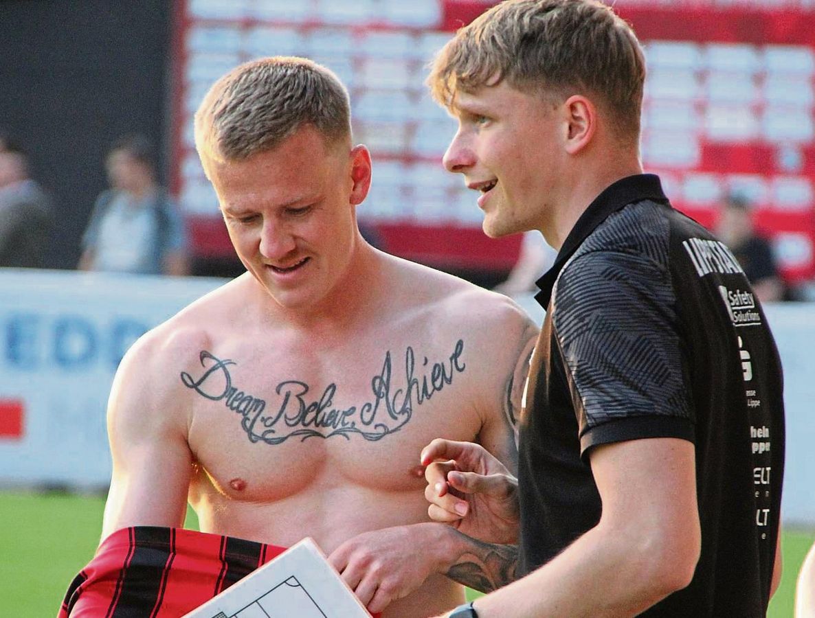 Dream. Believe. Achieve. Träume, glaube, erreiche – Lebe deine Träume und erreiche deine Ziele. Das Tattoo auf der Brust von Stürmer Gerrit Kaiser, hier mit Co-Trainer Maximilian Wallmeier, passt zur Situation des SV Lippstadt. Kleine Umwege sollten dabei erlaubt sein. Noch haben die Schwarz-Roten die Regionalliga nicht ganz abgehakt. Foto: Heinke