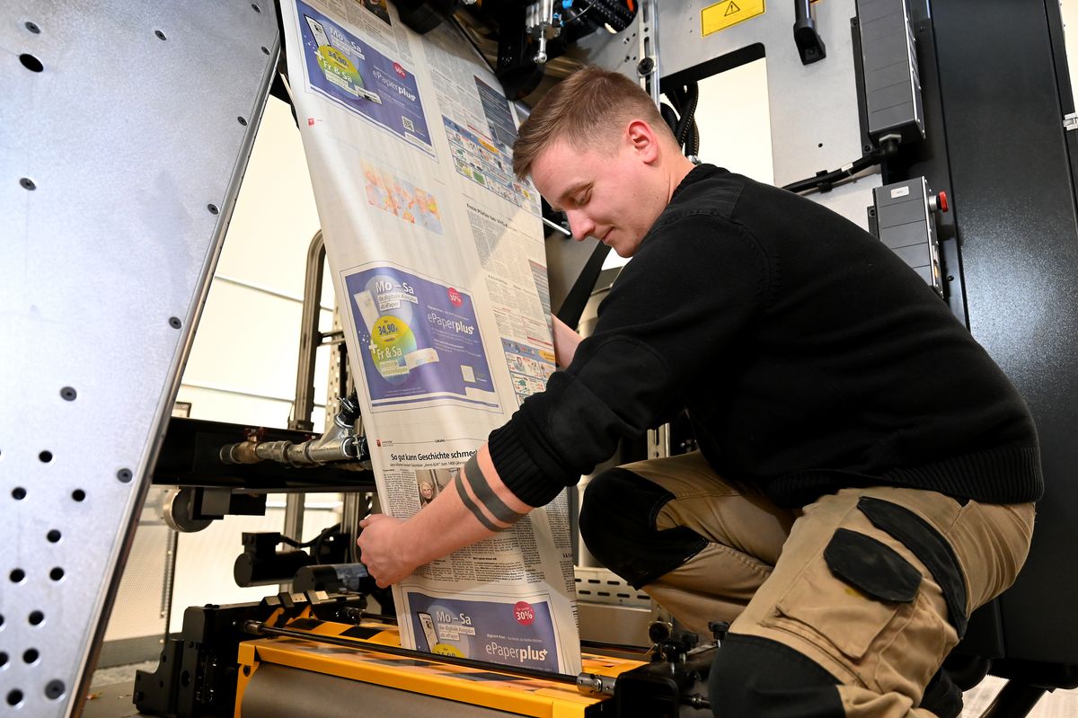 Die Zeitung wird gedruckt, geschnitten und gefaltet: Hendrik Lüllau zeigt für das Foto, wie die Papierbahn über einen Trichter läuft.
