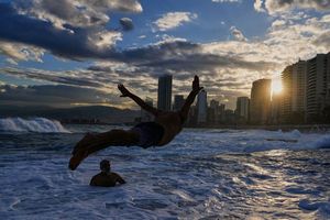 Ein Mann springt bei Temperaturen um die 10 Grad Celsius ins Mittelmeer, während die Sonne über Beirut aufgeht. - Foto: Hassan Ammar/AP/dpa