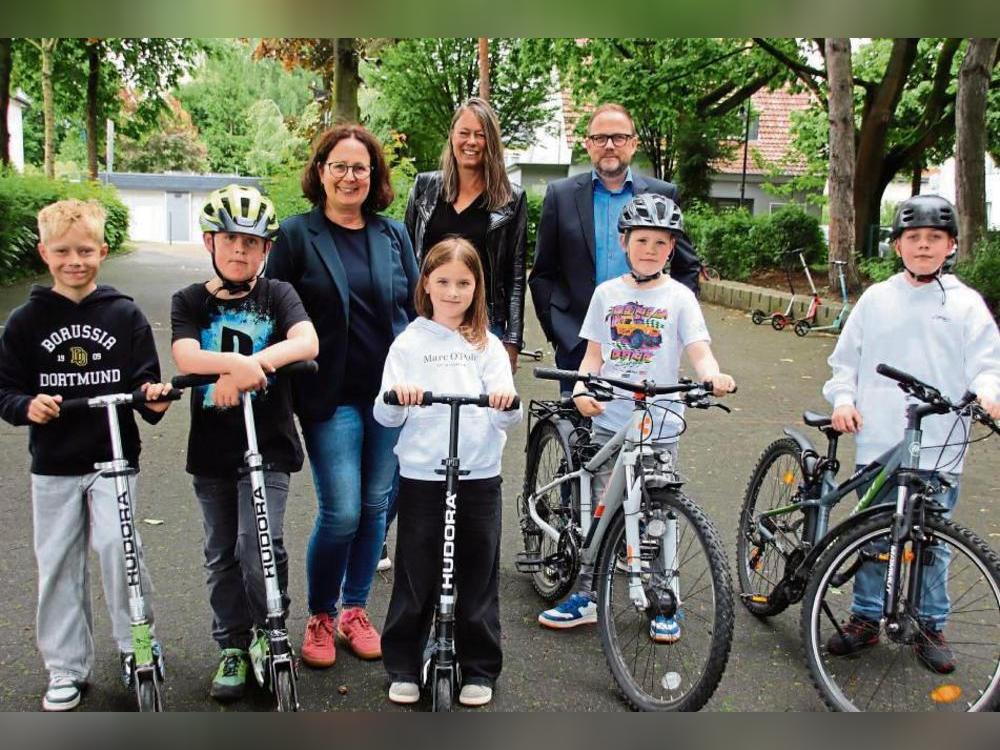 Schüler der Pankratius-Grundschule (vorne) sowie die Schulmobilitätsbeauftragte Petra Henke, Schulleiterin Sonja Kleine und Bürgermeister Alfred Schmidt (hinten, v.l.) freuen sich darüber, dass sie bald neue Fahrradständer für Roller und Räder erhalten. Foto: Meschede
