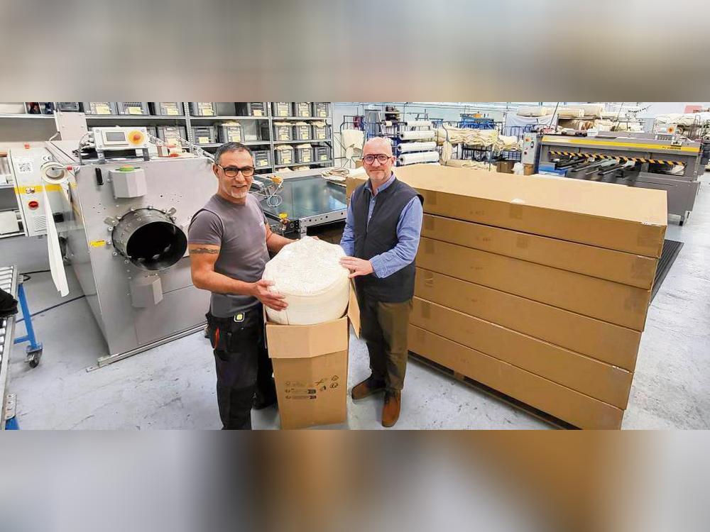 Die Roll-Pack-Anlage für Matratzen, hier gezeigt von Yacoub Gharib und Florian Kleinehollenhorst, reduziert das Versandvolumen um satte 60 Prozent gegenüber der herkömmlichen Verpackungsweise (rechts im Bild). Foto: Axel Schwade
