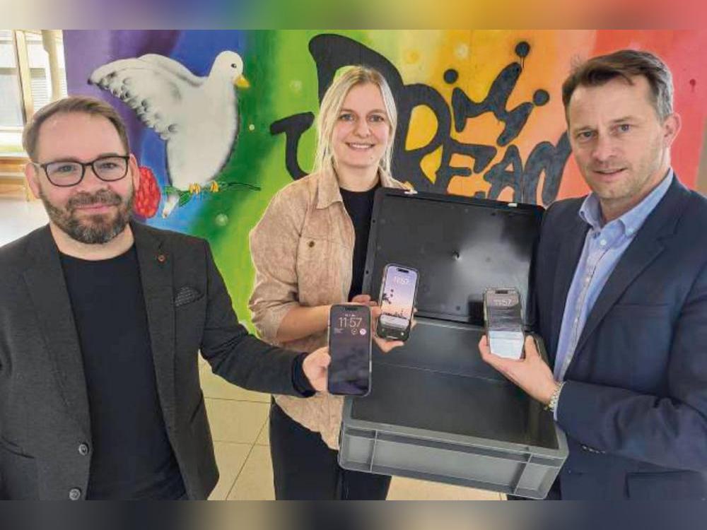 Wenn das Smartphone in eine Tresor-Kiste im Klassenraum kommt, können sich Schüler besser konzentrieren: Diese Erkenntnis aus einem Experiment erläuterten jetzt (v.l.) Prof. Sven Lindberg und Doktorandin Jeanette Skowronek dem Lippstädter Gesamtschul-Leiter Jan Haurand. Foto: Axel Schwade