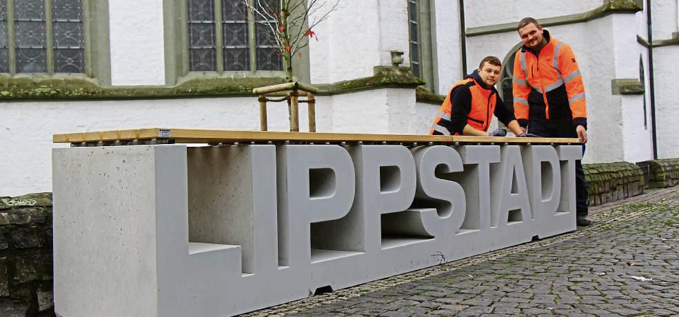 Bitte Platz nehmen: Die Bauhof-Mitarbeiter Marius Schneider (l.) und Timo Homberg montierten am Freitag die Holzauflage. Die Fotopoint-Lippstadt-Bank ist das Ergebnis eines Spendenprojektes unserer Zeitung zum 175. Patriot-Geburtstag im Jahr 2023. Foto: Löseke