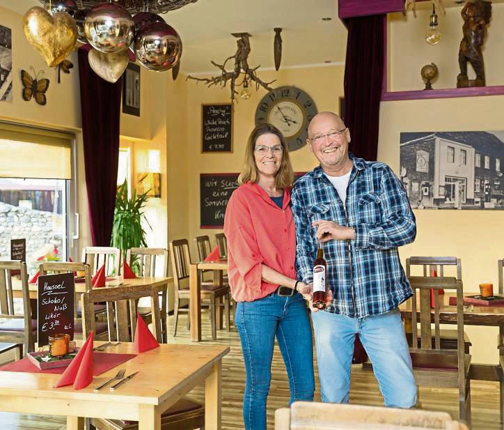 Axel „Acka“ Junker steht mit seiner Lebensgefährtin Tina Mackenzie und einer Flasche des selbst abgefüllten Hausöls im Wintergarten von Junker’s Restaurant. Dort befand sich früher eine Ausstellungsfläche für Yamaha-Motorräder. Foto: Gabi Bender