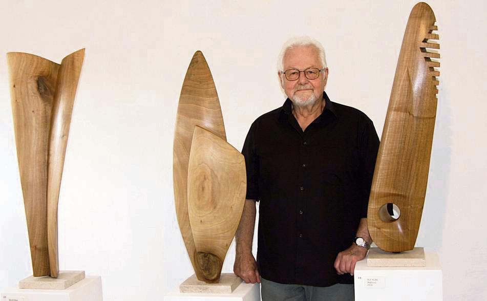 Karl-Heinz Reichhardt vor einer Figurengruppe, die seine Liebe zur natürlichen Form und die Herausarbeitung des Materials, in diesem Fall Walnuss, eindrucksvoll zeigt.