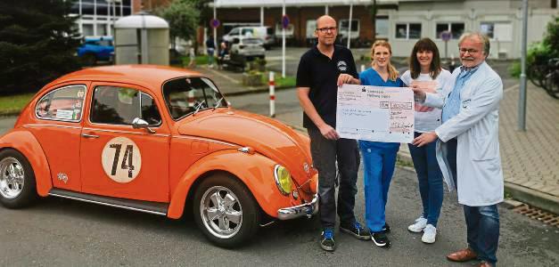Mit einem orange-farbenen Käfer überbrachten die Oldtimerfreunde den Spendenscheck.