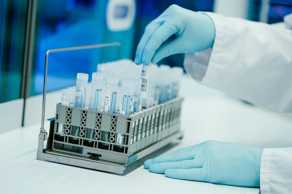 Ein Mitarbeiter hält in einem Coronatest-Labor PCR-Teströhrchen in den Händen. - Foto: Uwe Anspach/dpa
