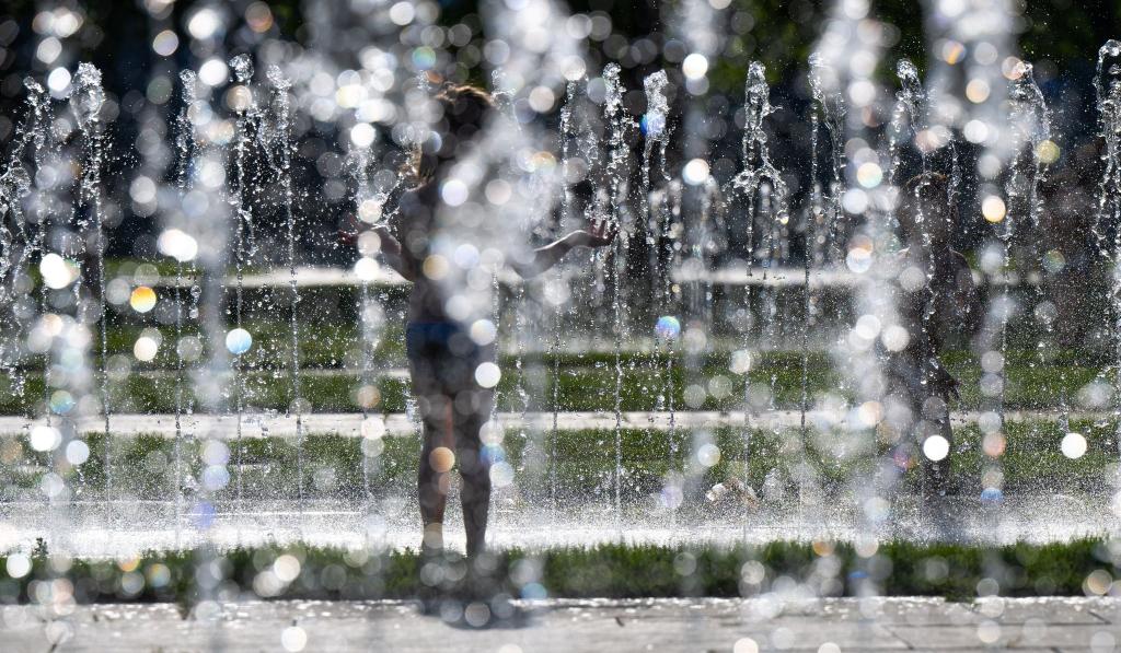 Kinder spielen bei sommerlichen Temperaturen am Springbrunnen vor dem Kanzleramt in Berlin. - Foto: Monika Skolimowska/dpa