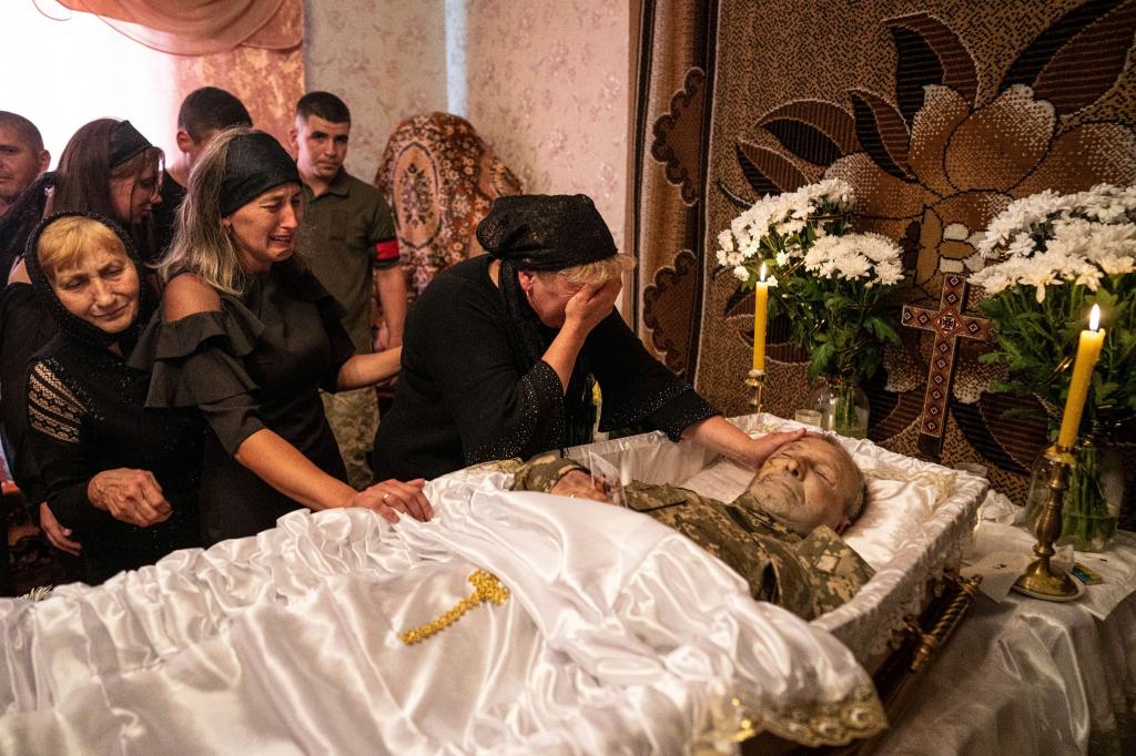 Eine Frau weint während der Trauerfeier am offenen Sarg ihres Mannes. Der ukrainische Soldat ist an der Front bei Kupjansk getötet worden. - Foto: Evgeniy Maloletka/AP/dpa