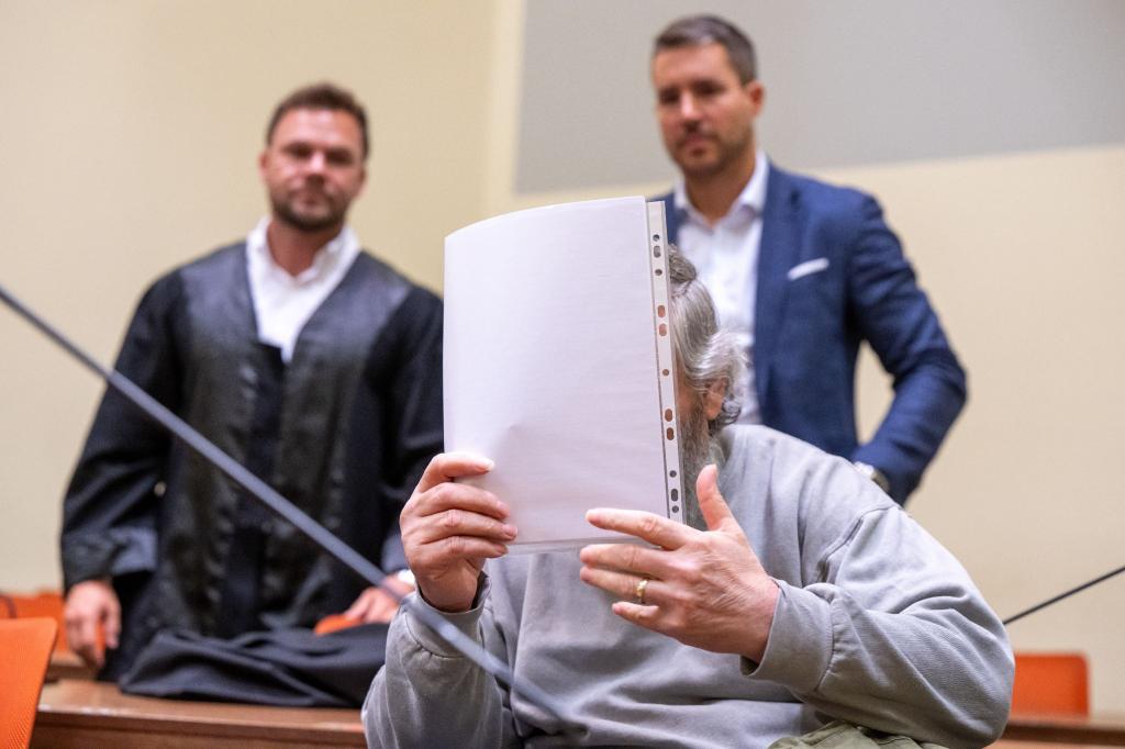 Der Angeklagte hält sich im Gerichtssaal ein Blatt Papier vor das Gesicht. Im Hintergrund stehen seine Anwälte. - Foto: Peter Kneffel/dpa