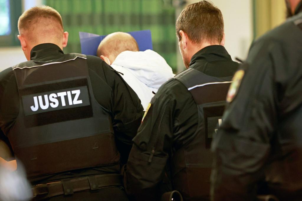 Der wegen Mordes angeklagte Mann (M) versteckt auf dem Weg in den Gerichtssaal sein Gesicht. - Foto: Matthias Bein/dpa