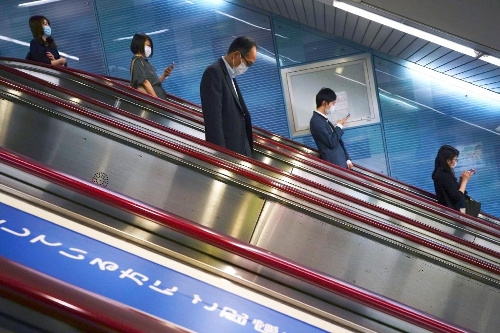 Menschen fahren auf einer Rolltreppe in eine U-Bahn-Station in Tokio. - Foto: Eugene Hoshiko/AP/dpa