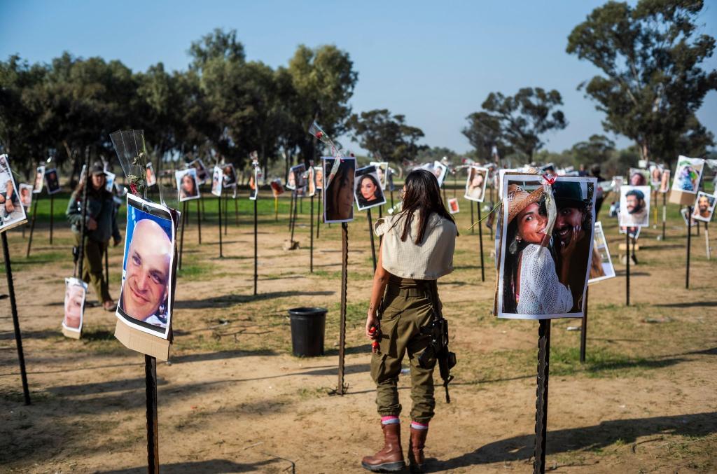 Israelische Soldatinnen stehen zwischen Fotos getöteter Israelis am Ort des Hamas-Massakers beim Musikfestival in der Negev-Wüste am 7. Oktober. - Foto: Ilia Yefimovich/dpa
