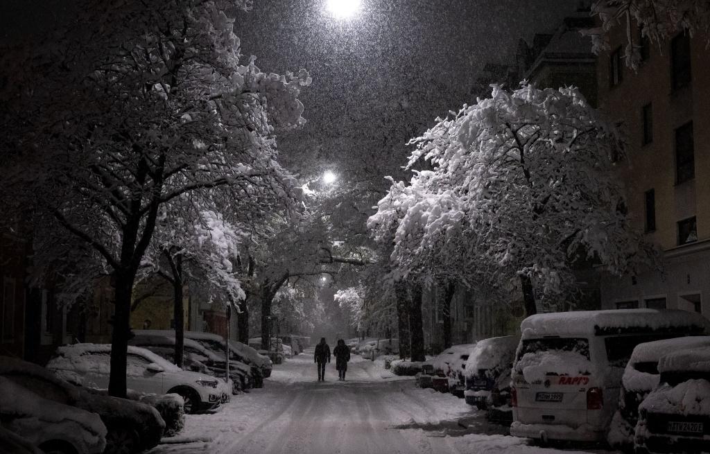 Der Winter ist in Deutschland angekommen. Bei einem abendlichen Spaziergang auf einer schneebedeckten Straße genießen zwei Passanten die weiße Pracht. - Foto: Sven Hoppe/dpa