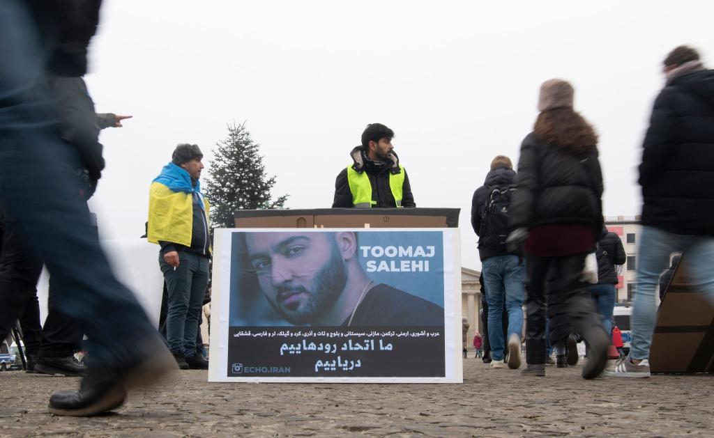 Protestaktion gegen Irans Staatsführung auf dem Pariser Platz in Berlin. Auf dem Plakat ist der Rapper Salehi zu sehen. - Foto: Paul Zinken/dpa
