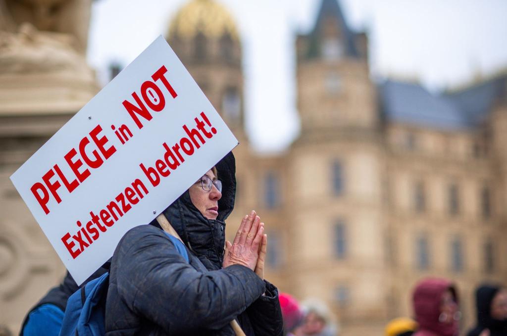 Bei einer Protestaktion vor dem Schweriner Landtag hält eine Teilnehmerin ein Schild mit der Aufschrift «Pflege in Not - Existenzen bedroht!». - Foto: Jens Büttner/dpa