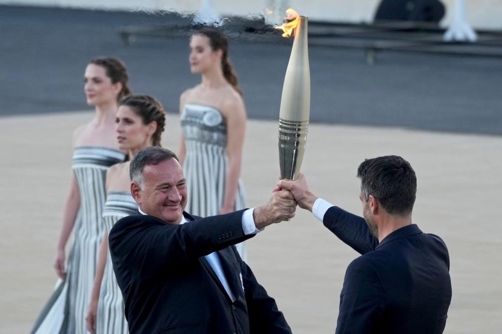 Der Präsident des französischen Organisationskomitees, Tony Estanguet (r), nahm die olympische Flamme in Athen entgegen. - Foto: Petros Giannakouris/AP/dpa
