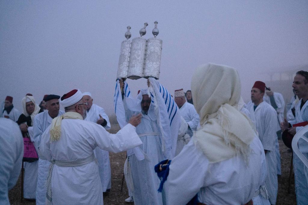 Ein Mitglied der samaritanischen Religionsgemeinschaft hält eine Tora-Schriftrolle hoch. Gäubige beten während der Pessach-Wallfahrt am Berg Garizim in Nablus. - Foto: Leo Correa/AP