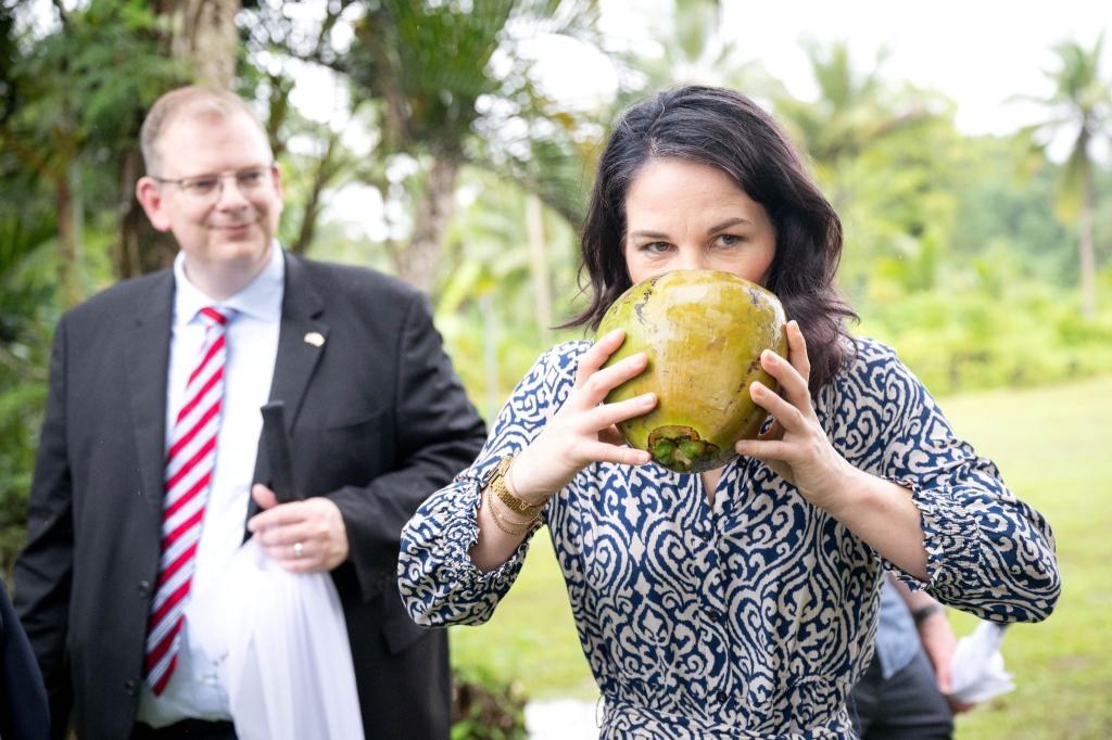 Die deutsche Außenministerin Annalena Baerbock trinkt aus einer Kokosnuss beim Besuch eines Dorfes im Klima-Krisengebiet Fidschi. - Foto: Sina Schuldt/dpa