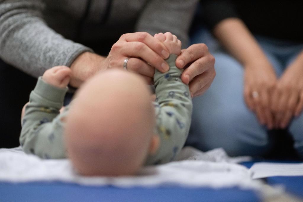 Ein Vater hält während eines Infant Handling Kurses die Füße seines Kindes, während die Mutter daneben sitzt. - Foto: Marijan Murat/dpa