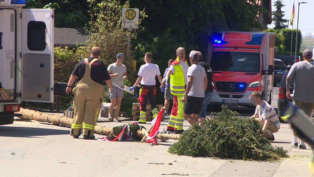 Der umgestürzte Maibaum liegt auf der Straße vor einem Einsatzwagen der Feuerwehr. - Foto: Guido Schulmann/TV-Niederrhein/dpa