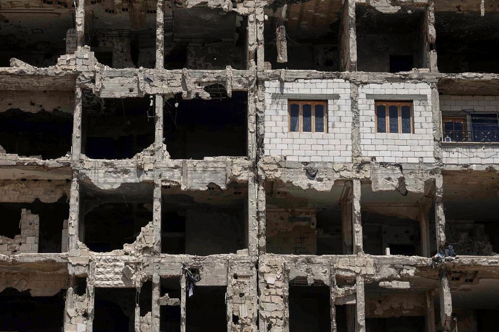 Die Wände und Fenster einer kürzlich restaurierten Wohnung ragen aus einem beschädigten Wohnhaus im vom Krieg zerstörten Viertel Al-Waer heraus. - Foto: Ghaith Alsayed/AP/dpa