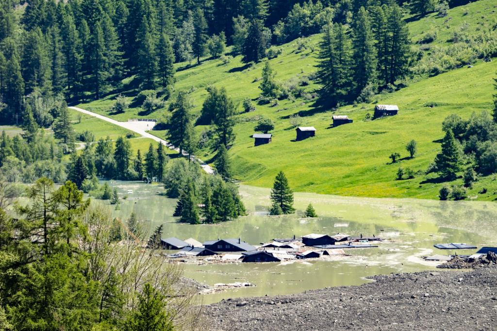 Nach Gletscherabbruch im Wallis: Nachdem sich ein See bei den letzten Häusern des Dorfes Blatten gebildet hat, fließt Wasser aus dem Fluss Lonza über Schlamm und Steine. - Foto: Jean-Christophe Bott/KEYSTONE/dpa