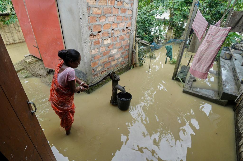 Eine Frau versucht in der überfluteten Umgebung ihres Hauses, Wasser zu sammeln. - Foto: Uncredited/AP/dpa