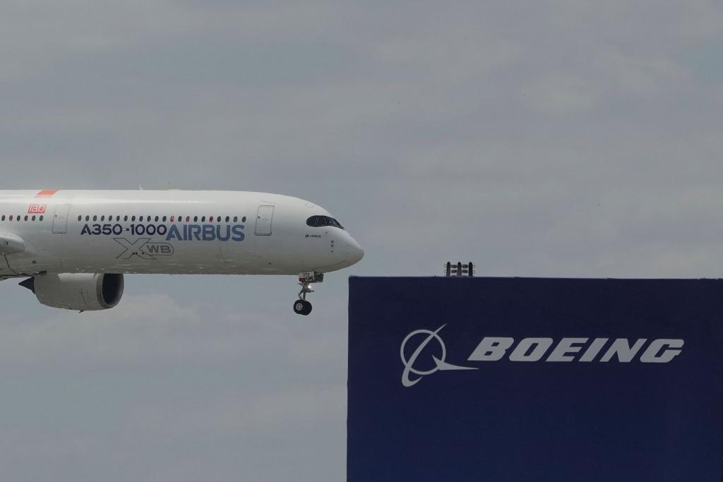 Die zwei großen Konkurrenten: Ein Airbus fliegt bei einer Vorführung auf der Luftfahrtmesse Salon du Bourget an einem Logo von Boeing vorbei. - Foto: Michel Euler/AP/dpa