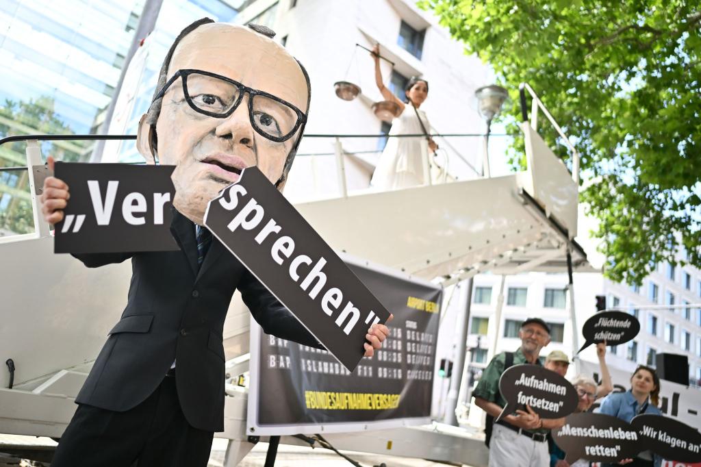 Ein Aktivist mit Merz-Maske zerbricht während einer symbolischen Protestaktion von Kabul Luftbrücke und Campact ein Schild mit der Aufschrift «Versprechen». - Foto: Sebastian Christoph Gollnow/dpa