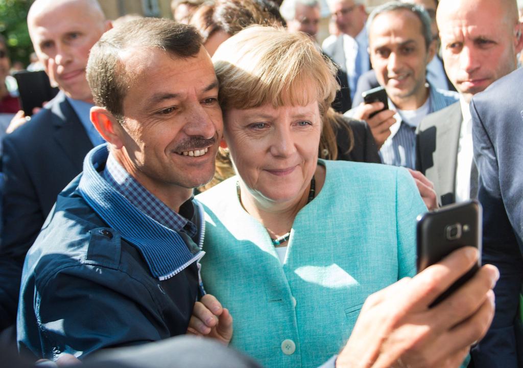 Bald zehn Jahre her: Angela Merkel (CDU) lässt sich nach dem Besuch einer Erstaufnahmeeinrichtung für Asylbewerber in Berlin-Spandau für ein Selfie zusammen mit einem Flüchtling fotografieren. (Archivbild) - Foto: Bernd von Jutrczenka/dpa