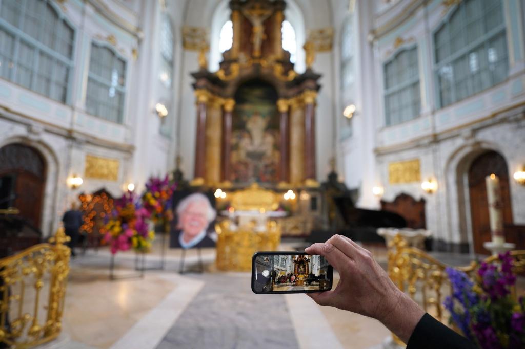 Ein Besucher macht zu Beginn der Trauerfeier ein Foto mit einem Smartphone. - Foto: Marcus Brandt/dpa