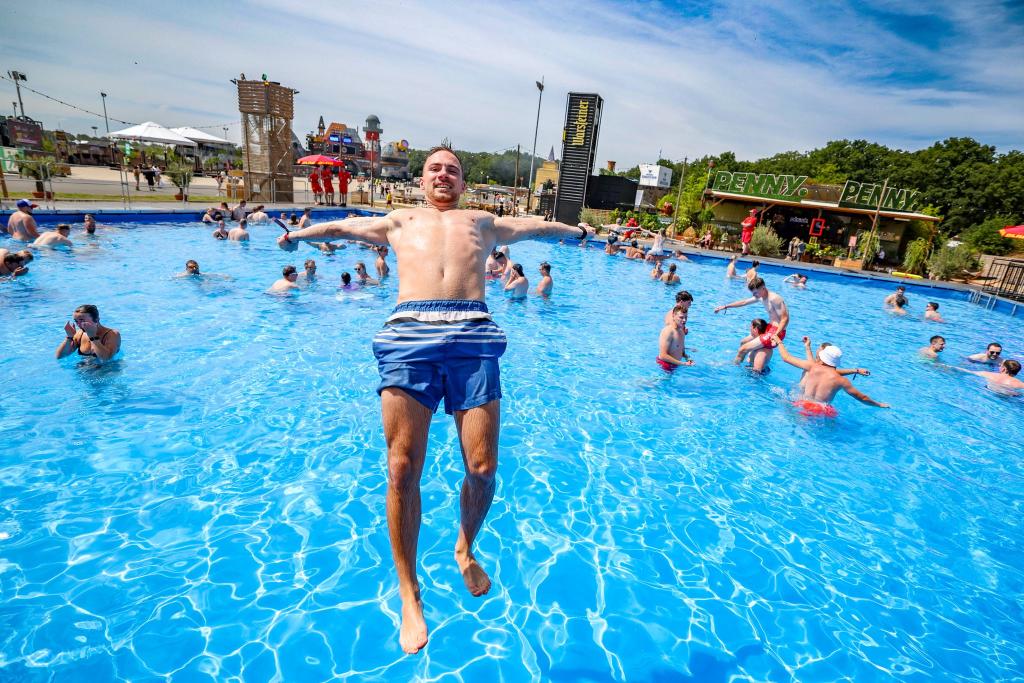Niklas H.aus Heideburg in Rheinland-Pfalz springt bei sommerlichen Temperaturen rückwärts in den großen Pool auf dem Festivalgelände. - Foto: Christoph Reichwein/dpa