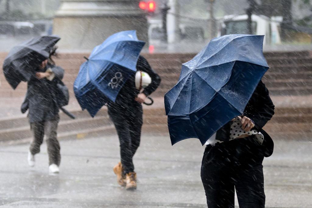 Auch in Australien scheint nicht immer die Sonne: Passanten in Sydney schützen sich mit Schirmen vor starkem Regen. - Foto: Steve Markham/AAP/dpa