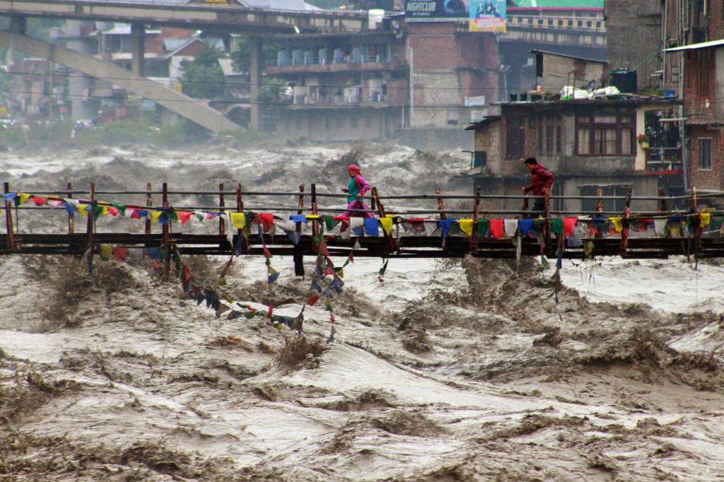 Menschen wagen im nordindischen Bundesstaat Himachal Pradesh trotz schwerer Überschwemmungen den Weg über eine Brücke, um den Fluss Beas zu überqueren. - Foto: Aqil Khan/AP/dpa