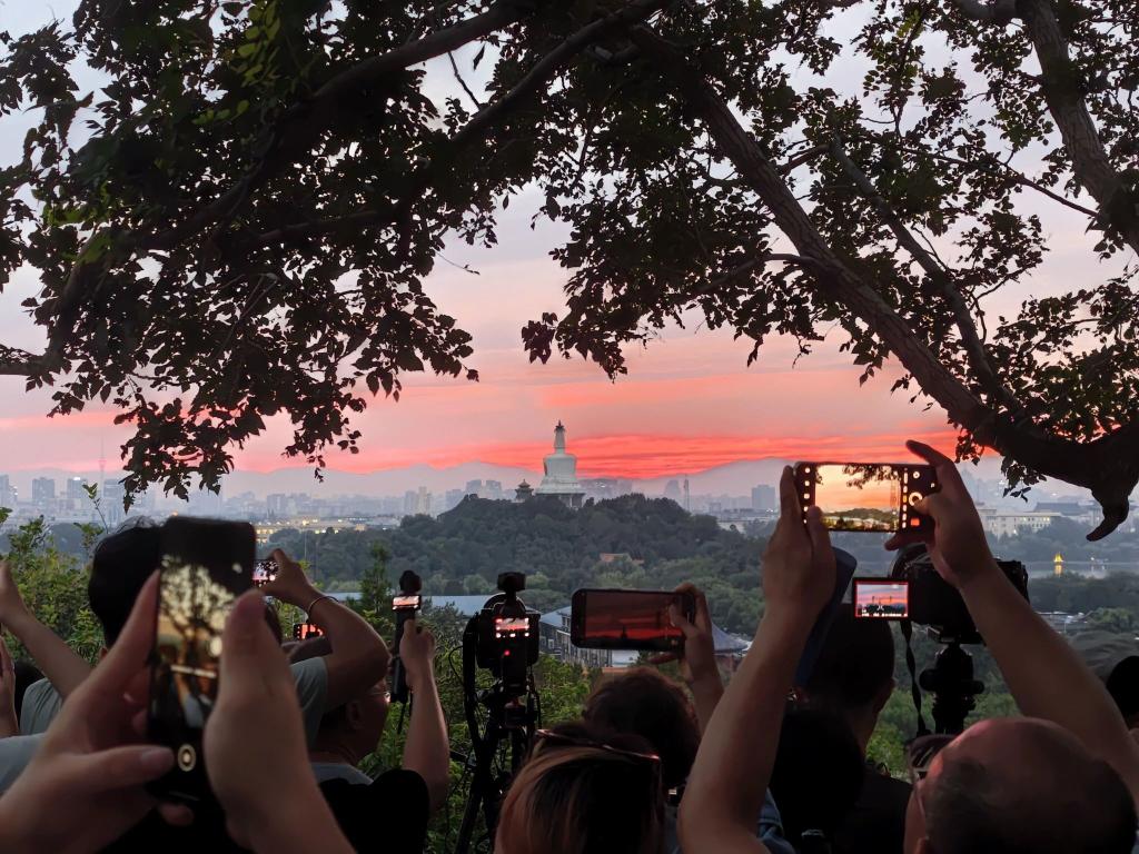 Touristen fotografieren mit ihren Handys den farbenfrohen Sonnenuntergang über der chinesischen Hauptstadt. - Foto: Xing Guangli/XinHua/dpa