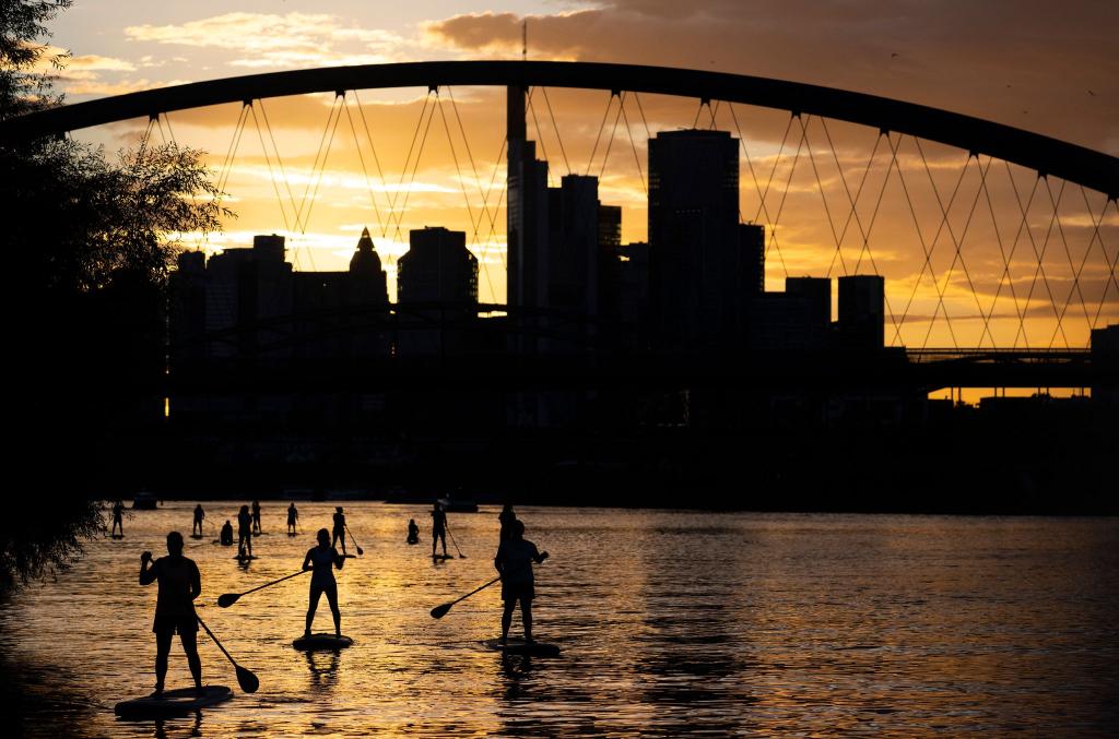 Bei Sicht auf die Skyline im letzten Licht des Tages fahren Stand-Up-Paddler in Nähe der Frankfurter Osthafenbrücke über den Main. - Foto: Boris Roessler/dpa