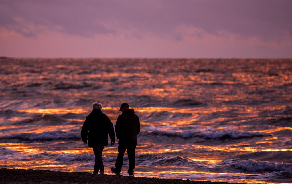 Spaziergänger sind nach Sonnenuntergang am Strand von Warnemünde an der Ostsee unterwegs. - Foto: Jens Büttner/dpa