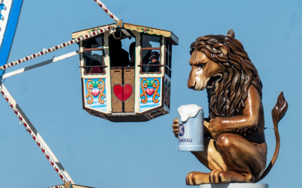Wiesn-Besucher fahren in einem Riesenrad auf dem 190. Münchner Oktoberfest an der Kulisse einen überdimensionalen Löwen mit Bierkrugs vorbei. - Foto: Peter Kneffel/dpa