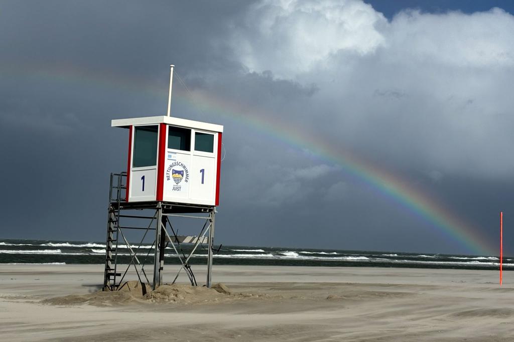 Ein Regenbogen steht an einem Himmel voll dunkler Wolken über der Nordsee und über der Insel Juist. - Foto: Federico Gambarini/dpa