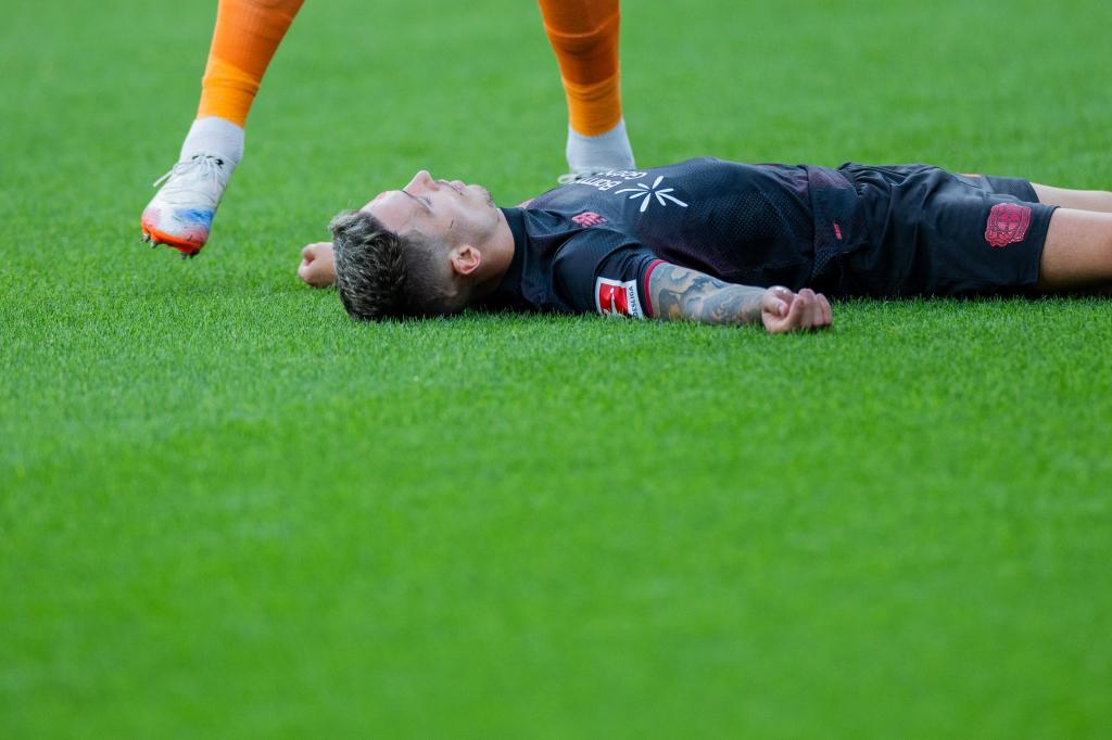 Bayer Leverkusens Kapitän Alejandro Grimaldo liegt nach einem Zusammenprall mit dem eigenen Mann benommen auf dem Boden. - Foto: Rolf Vennenbernd/dpa
