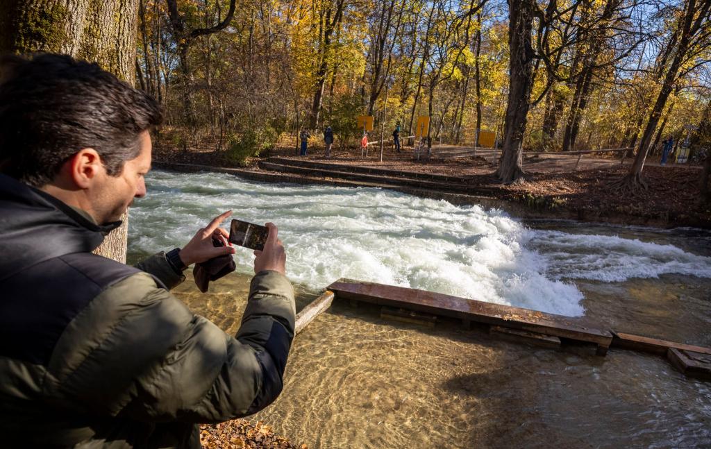 Freizeitsurfer Alexander Neumann fotografiert die - zurzeit nicht funktionstüchtige - Eisbachwelle im Englischen Garten. - Foto: Peter Kneffel/dpa