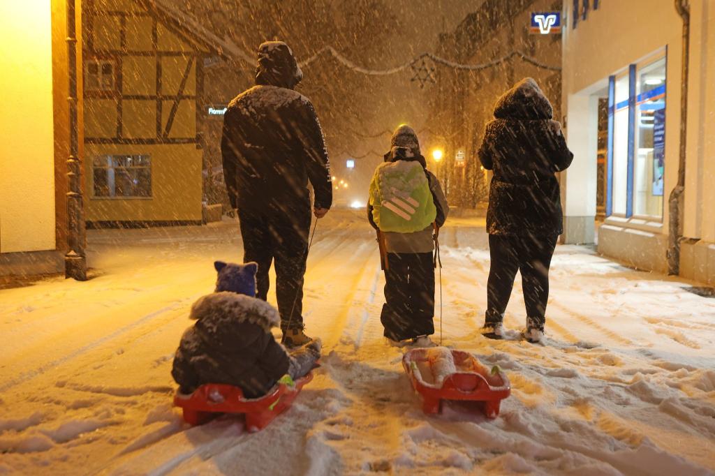 Eltern bringen am frühen Morgen in Wernigerode ihre Kinder mit Schlitten in die Schule. Wintersturm «Elli» bringt Eiseskälte, Glätte und viel Schnee, so dass Busse und Bahnen teils nur eingeschränkt unterwegs sind. - Foto: Matthias Bein/dpa