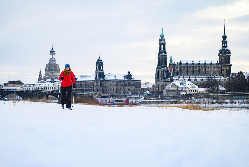 Eine Frau läuft am verschneiten Elbufer vor der historischen Altstadtkulisse in Dresden Ski - Foto: Robert Michael/dpa