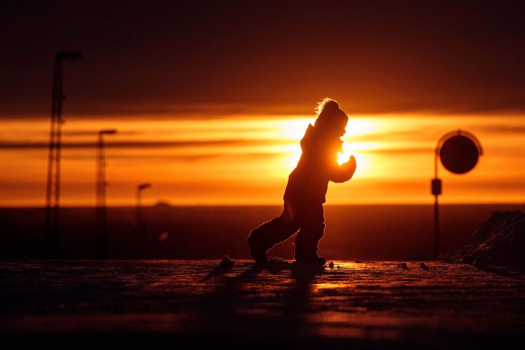 Ein Junge läuft bei Sonnenuntergang über eine Straße in Nuuk in Grönland. - Foto: Evgeniy Maloletka/AP/dpa